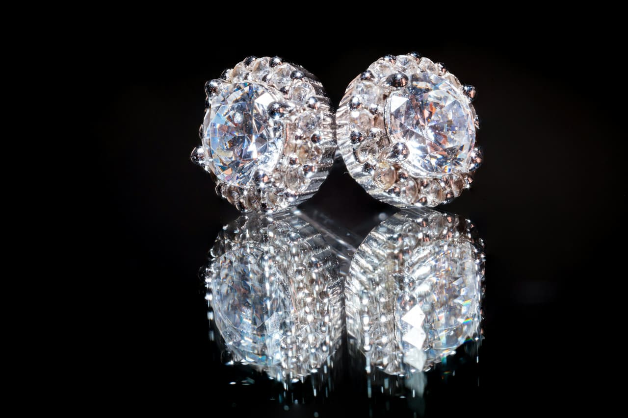 A pair of diamond stud earrings reflected on a black surface